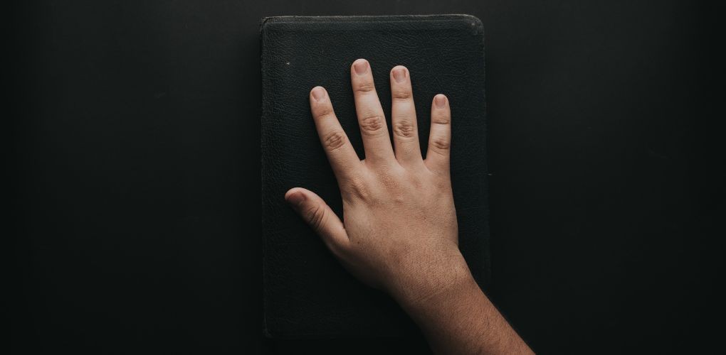 Une main posée sur un livre noir.