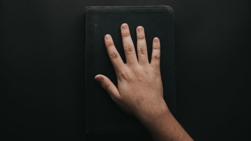 Une main posée sur un livre noir.
