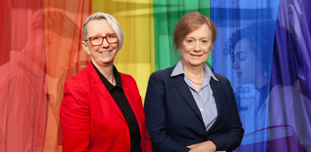 Marie Laure Leclercq et Matine Roy, membre de la Commission des droits. À l’arrière, le drapeau arc-en-ciel à travers lequel on distingue des personnes qui discutent.