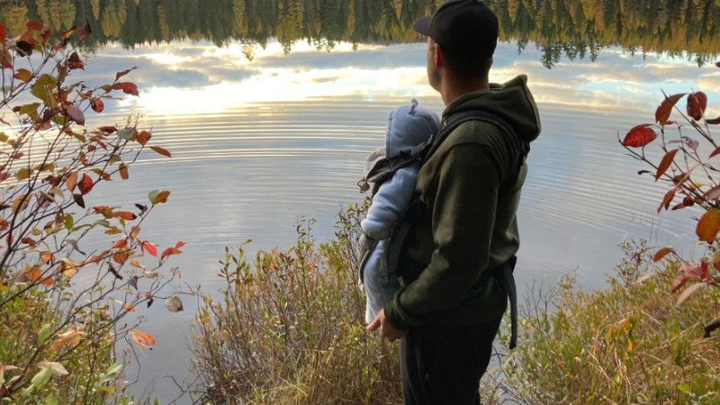 Un père et son bébé regardent un lac en automne.