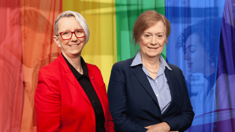 Marie Laure Leclercq et Matine Roy, membre de la Commission des droits. À l’arrière, le drapeau arc-en-ciel à travers lequel on distingue des personnes qui discutent.