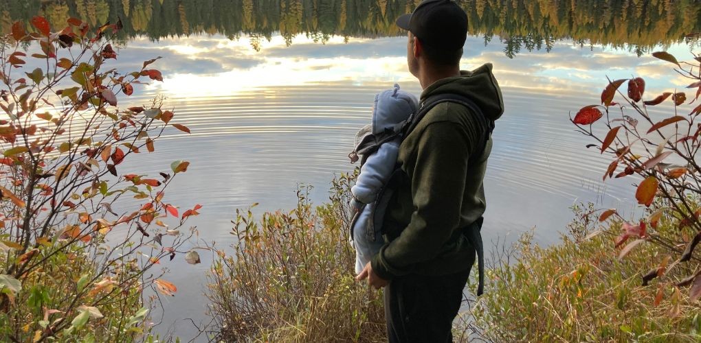 Un père et son bébé regardent un lac en automne.