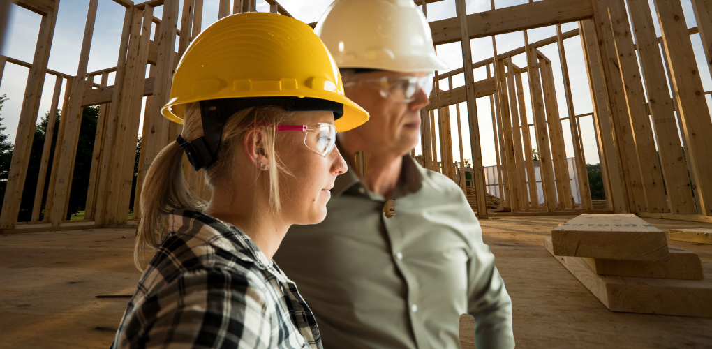 Une femme et un homme sur un chantier de construction. On voit la charpente du bâtiment derrière les personnes.