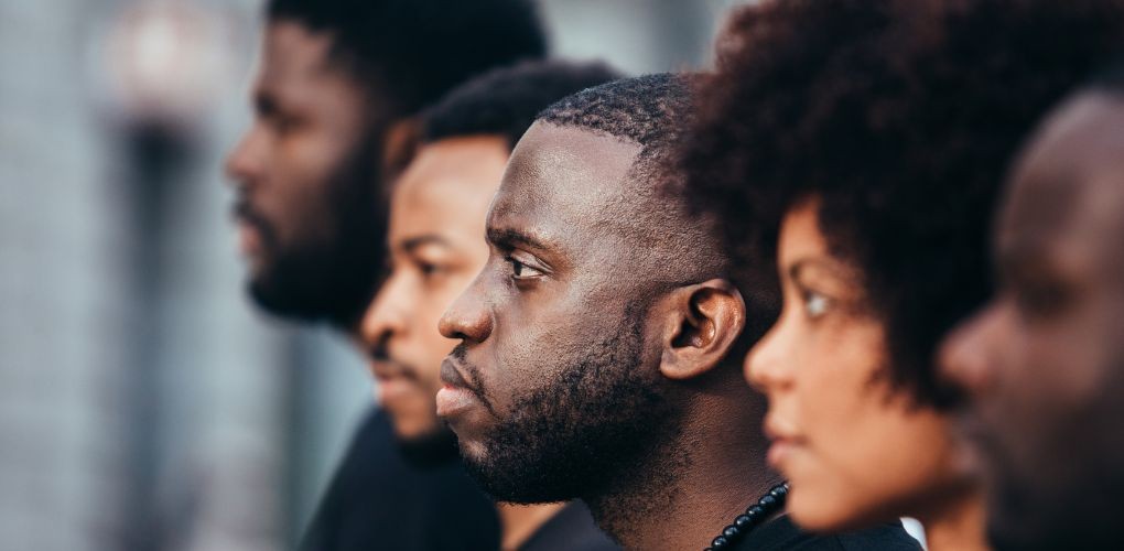 Une femme et des hommes noirs vus de profil regardent au loin.