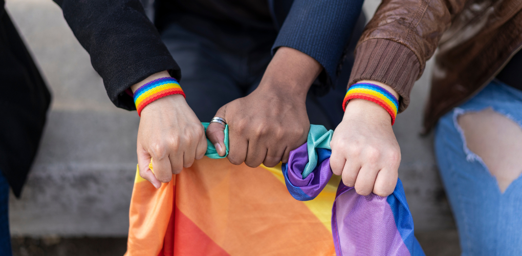 Une photo de trois mains tenant le drapeau arc-en-ciel.